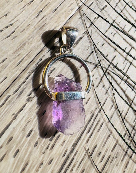 Amethyst crystal pendant with gold and silver accents on a wooden surface