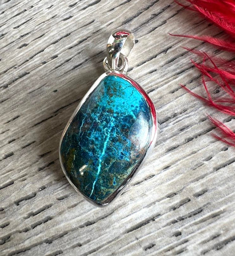Blue stone pendant on a silver chain with red fabric in the background