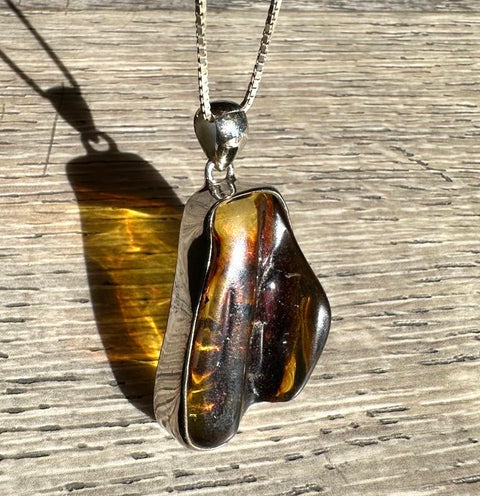 Pendant with tiger's eye stone on a silver chain against a wooden background