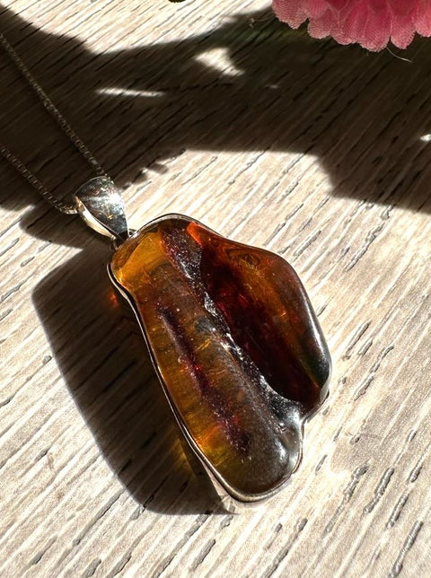 Amber pendant on a wooden surface with a pink flower in the corner