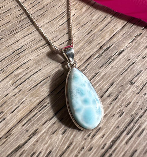 Teardrop-shaped larimar pendant on a silver chain against a wooden background