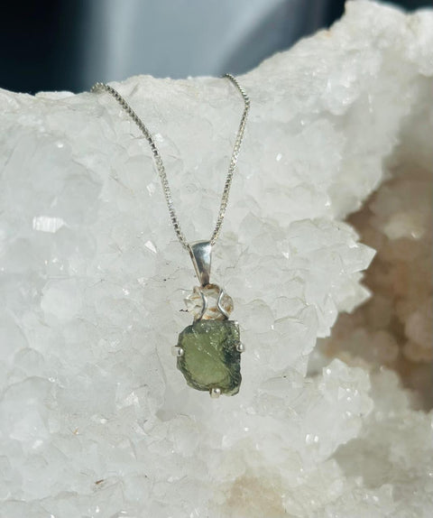 Green crystal pendant on a silver chain against a white crystal background