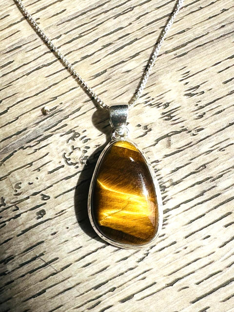 Tiger's eye pendant on a silver chain against a wooden background