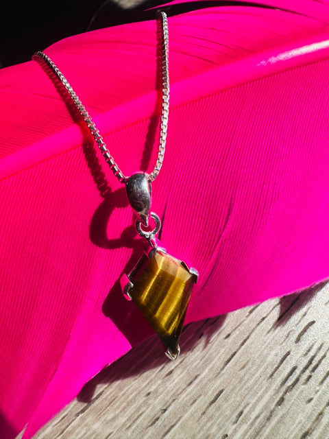 Necklace with a tiger's eye pendant on a pink surface